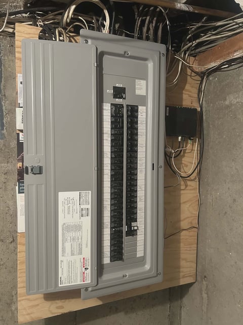 Open electrical panel box mounted on wooden surface showing circuit breakers and wiring